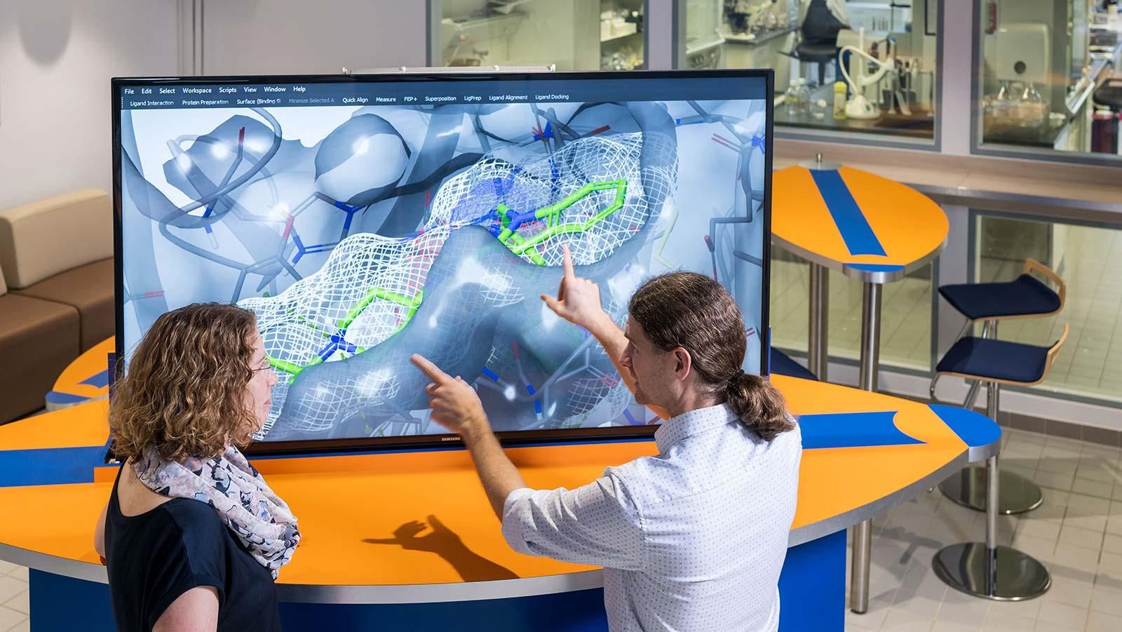 Zwei Forschende am BioCampus von Sanofi schauen sich ein Moleküldesign auf einem großen Screen an