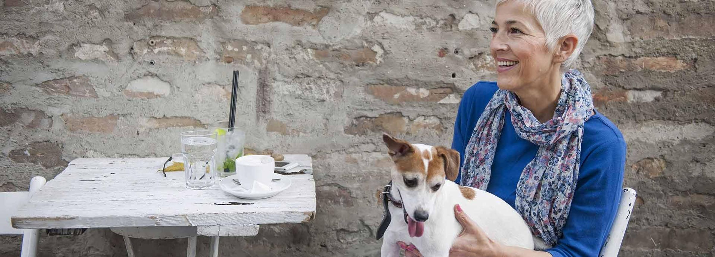 Frau sitzt mit ihrem Hund an einem Tisch und trinkt einen Kaffee